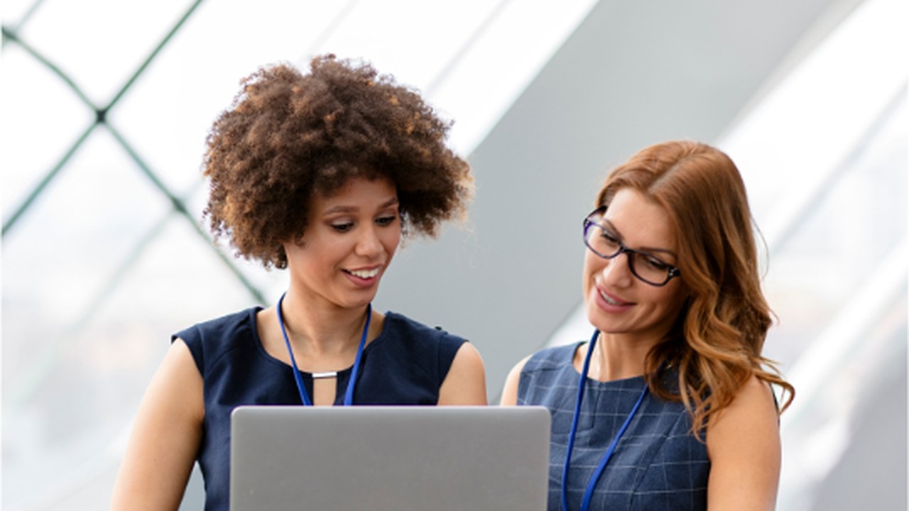 Two women business colleagues smiling as they review work on a laptop together